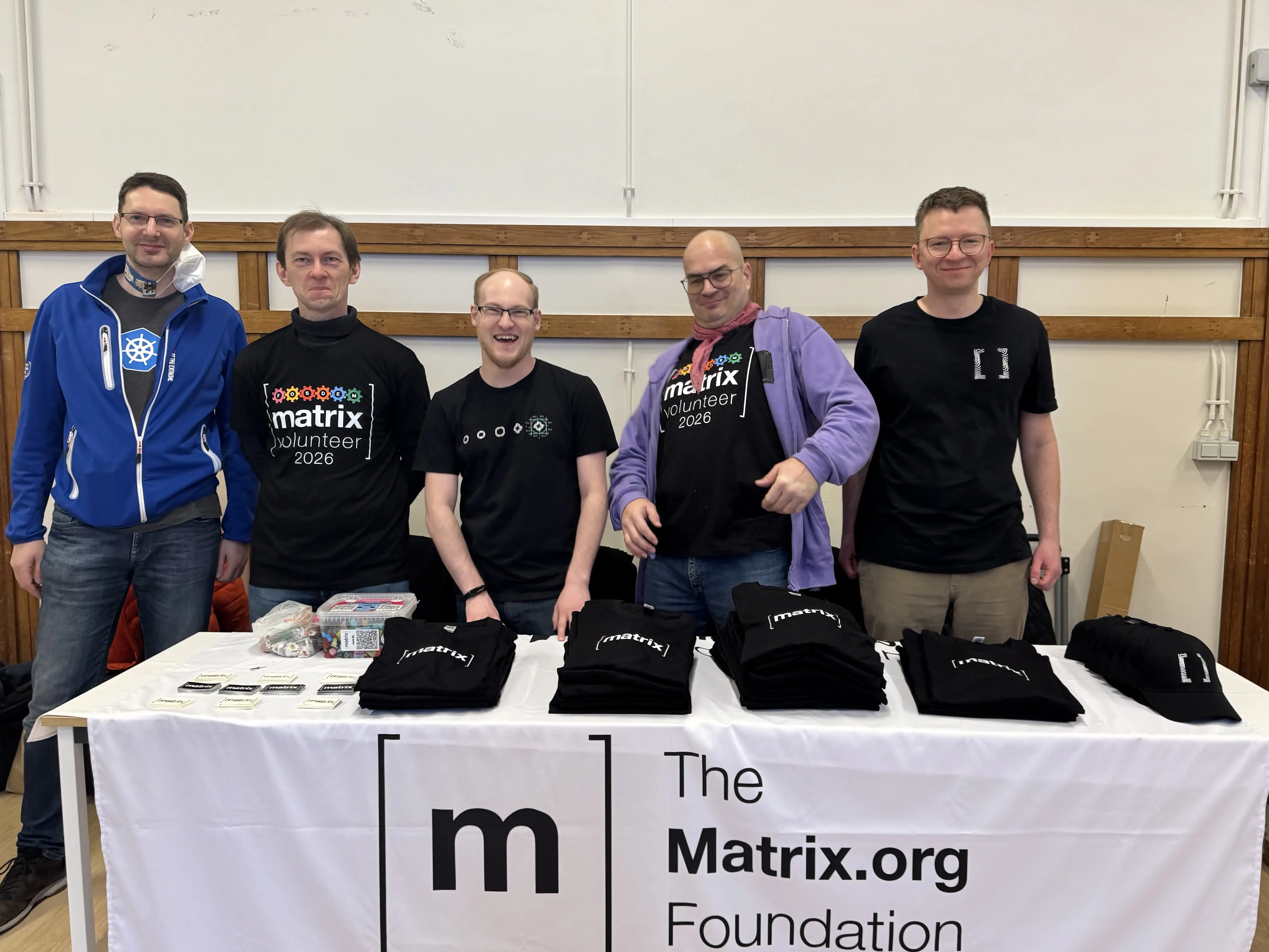 A team of people making goofy faces and laughing, behind a Matrix.org Foundation branded booth.
